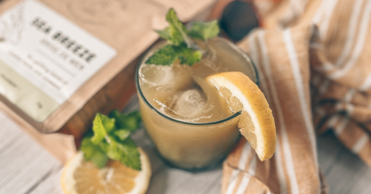 Elixir Mocktails for Summer Wellness. Image features a glass of the Matcha Mind Mojito recipe next to a bag of Harmonic Arts Sea Breeze Artisan Tea.